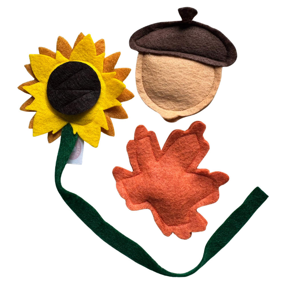 Felt autumn-themed accessory set featuring a yellow sunflower with a dark brown center and green stem, a brown acorn cap with a beige body, and an orange leaf, all on a plain white background.