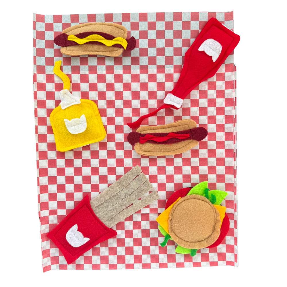 BBQ themed catnip toys with cheeseburger, hot dogs, fries, ketchup, and mustard on picnic paper for interactive cat play