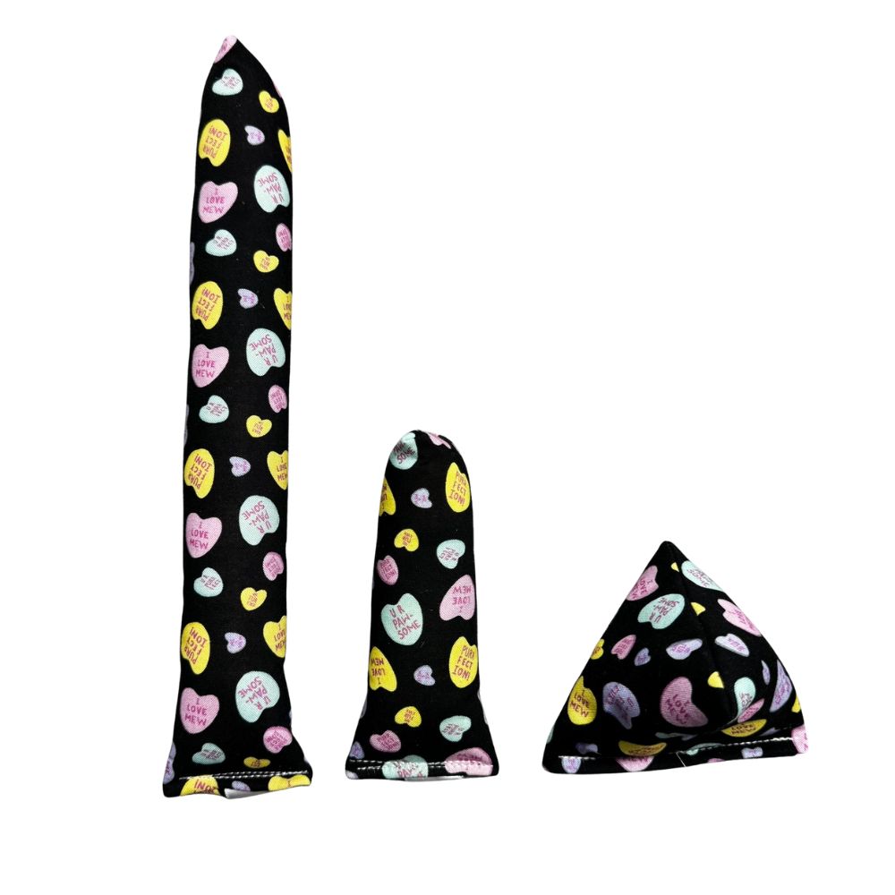 Group photo of handmade cat toys including a full-size kicker, mini kicker, and Happy Sack in black fabric with pastel candy hearts, filled with signature premium catnip. Made by CatnipTakeout.