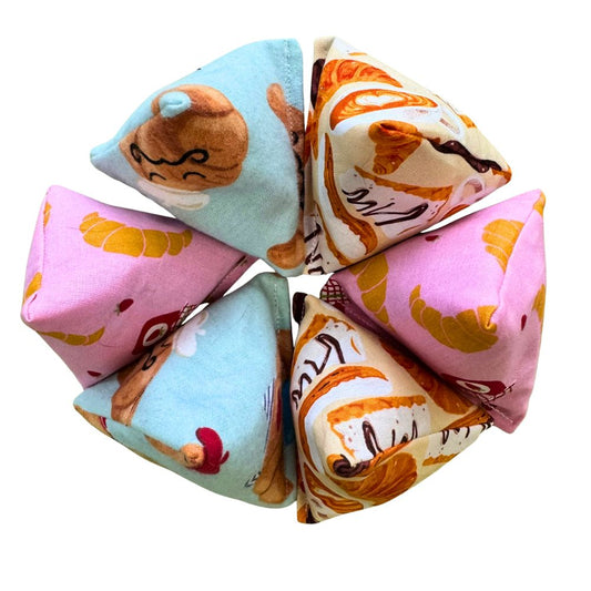 Croissant-themed Happy Sack catnip cat toy from CatnipTakeout, featuring a pyramid-shaped design made with playful croissant print fabrics in pink, cream, and light blue, paired with a felt croissant accent. This interactive cat toy is designed for kittens and playful cats who love batting, tossing, pouncing, and food-inspired enrichment.