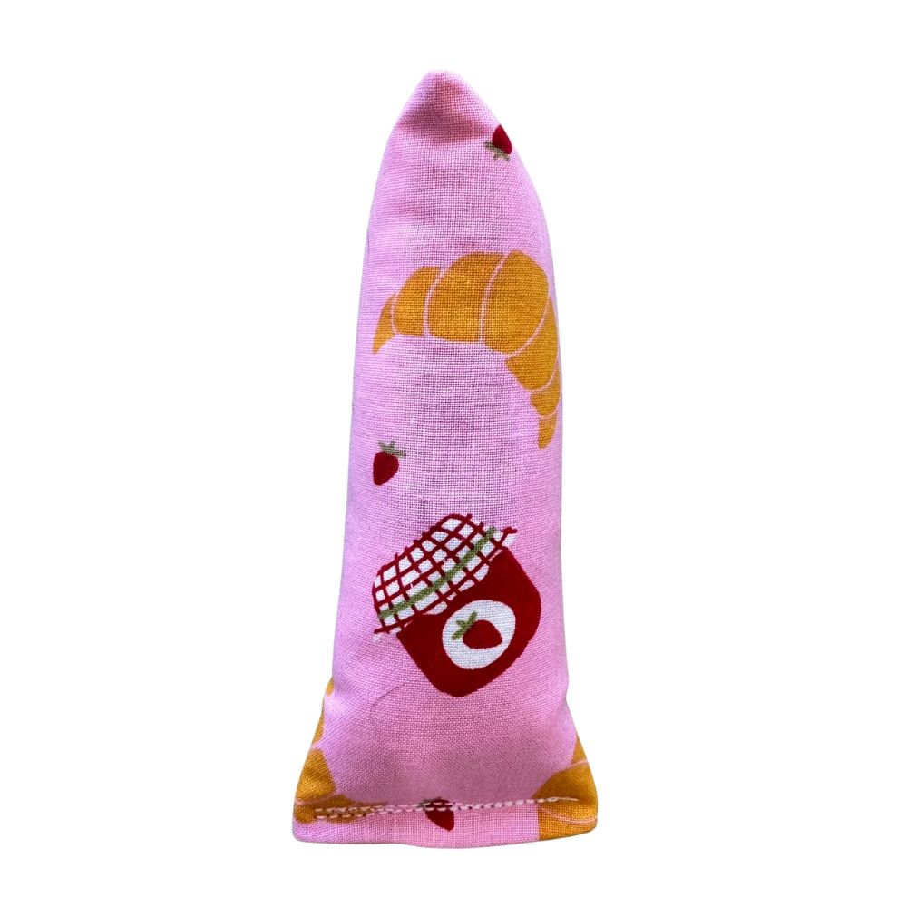 CatnipTakeout Croissant Mini Kicker Catnip Toy shown in a slim, elongated mini kicker shape designed for kittens and adult cats. Features pink bakery-themed fabric with illustrated croissants, strawberries, and jam jars. Durable construction sized for easy gripping, bunny kicks, and solo play, filled with CatnipTakeout’s signature aromatic catnip for long-lasting engagement.