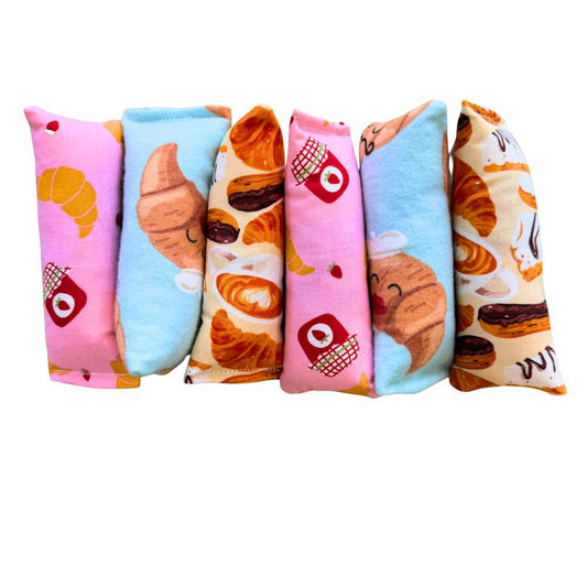 Assorted CatnipTakeout Croissant Mini Kicker Catnip Toys displayed side by side, showing multiple fabric variations in the croissant bakery theme. Slim, elongated mini kicker shape designed for kittens and adult cats to grab, bunny-kick, and bat during solo or interactive play. Fabrics include pink and blue pastry prints with illustrated croissants, jam jars, strawberries, and café-style details. Each mini kicker is filled with CatnipTakeout’s signature aromatic catnip for engaging, self-directed play.