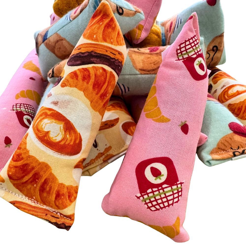 Group of CatnipTakeout Croissant Mini Kicker Catnip Toys arranged together, showing multiple croissant-themed fabric designs. Slim mini kicker shape is perfect for kittens and small cats who enjoy solo play, grabbing, carrying, and bunny-kicking. Fabrics feature illustrated croissants, jam jars, strawberries, café drinks, and pastry details in soft pinks, blues, and warm bakery tones. Filled with CatnipTakeout’s signature aromatic catnip to encourage independent, engaging play.