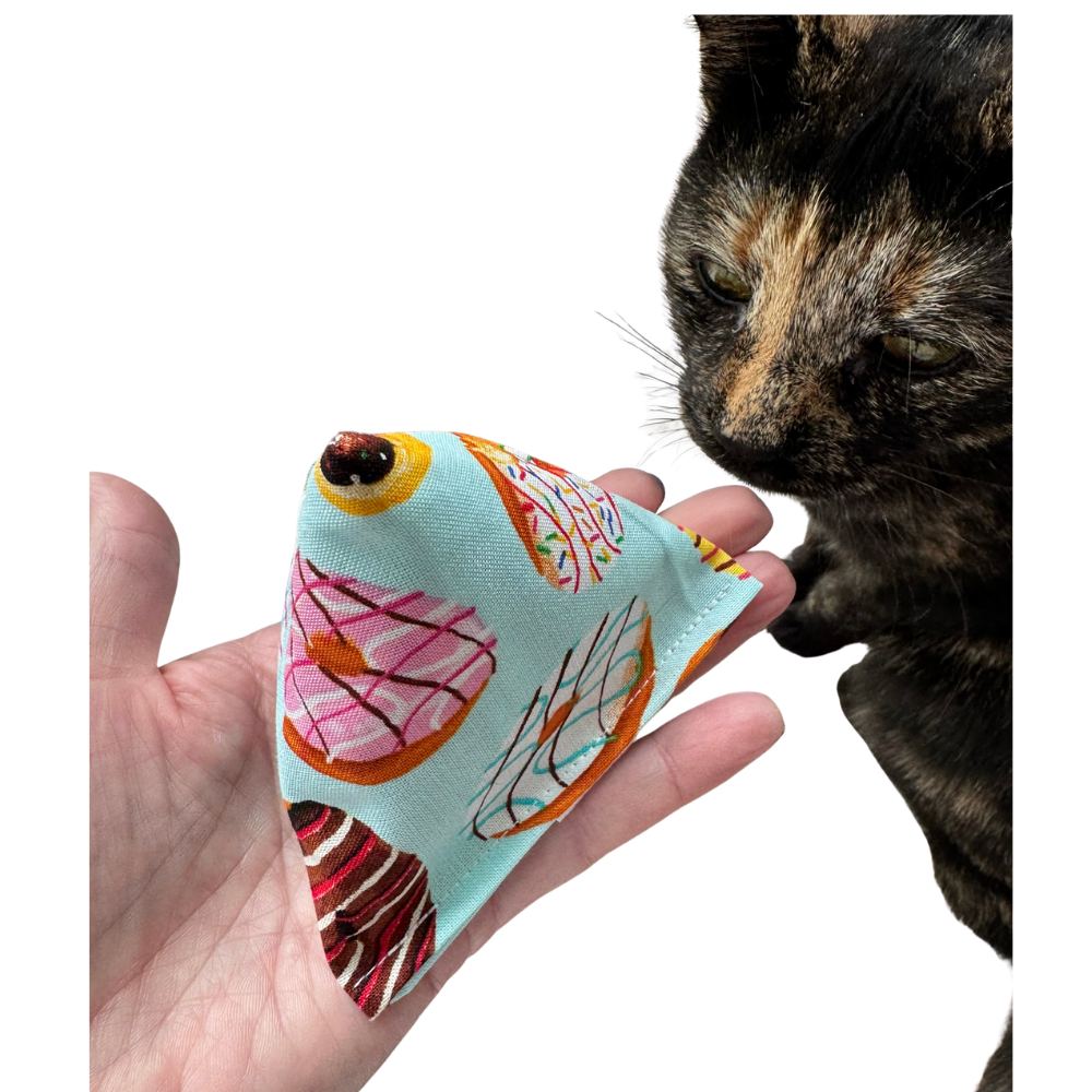 Donut cat toy Happy Sack shown in hand beside a tortoiseshell cat for size and cat-approved play