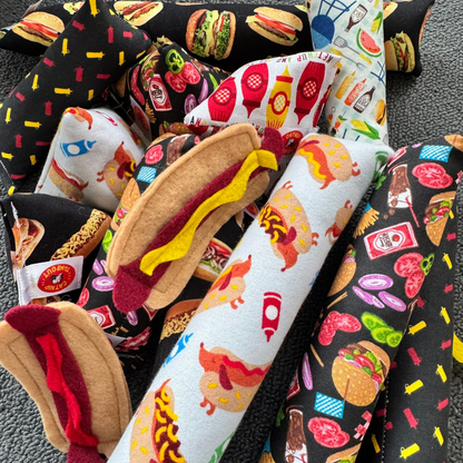 Felt hot dog cat toys beside catnip kickers with burgers, ketchup bottles, mustard bottles, and grilling inspired foodie themes