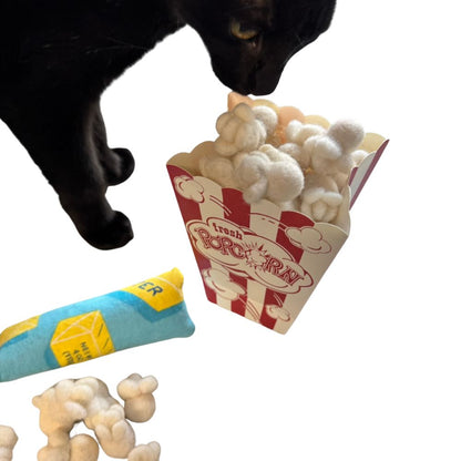 Black cat sniffing a popcorn-themed cat toy with plush popcorn pieces in a striped popcorn box, sprayed with catnip and shown during interactive play