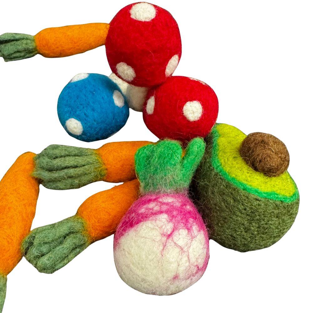 Close-up image of an avocado-shaped cat toy with layered green tones and brown pit alongside a round pink-and-white radish and carrots. Emphasizes shape and color contrast. Made by CatnipTakeout