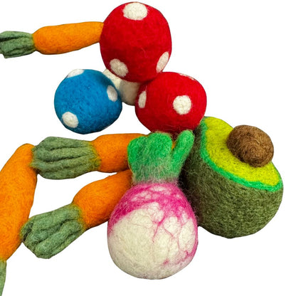 Close-up image of an avocado-shaped cat toy with layered green tones and brown pit alongside a round pink-and-white radish and carrots. Emphasizes shape and color contrast. Made by CatnipTakeout