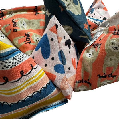 Close-up photo of multiple handmade Sloth Happy Sack cat toys showing fabric textures and prints, pyramid shape designed for batting and pouncing, filled with signature premium catnip. Made by CatnipTakeout.