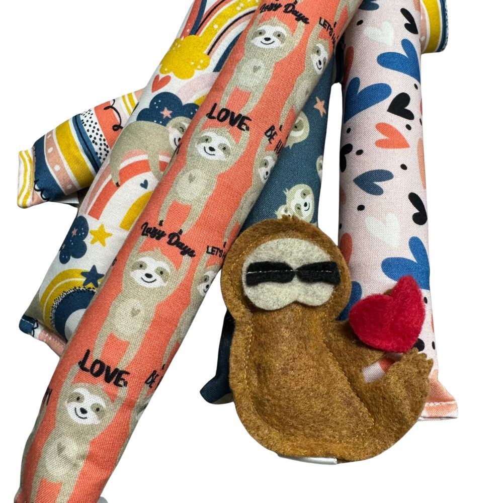 Handmade sloth kicker and Happy Sack cat toys shown together in five Valentine sloth prints, filled with signature premium catnip and designed for kicking, pouncing, and cozy play. Made by CatnipTakeout.