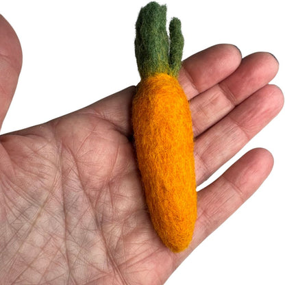 Hand holding a felt carrot toy with green leaves on a white background