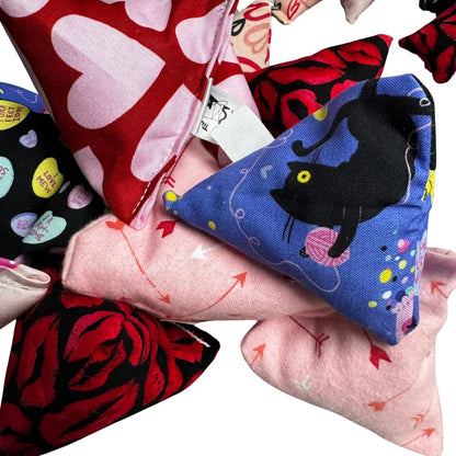 Close-up group photo of handmade Valentine cat toys including heart kickers, arrow-pattern Happy Sacks, rose designs, and playful cat motifs, all filled with signature premium catnip. Made by CatnipTakeout