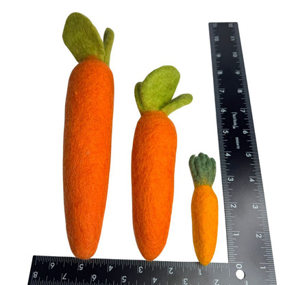 Three wool carrot cat toys orange with green tops on a white background with a ruler for scale.