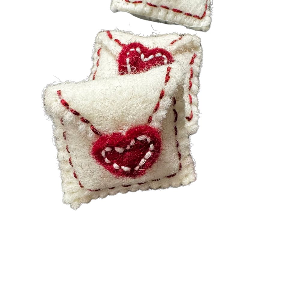 Two handmade white wool love-letter envelope cat toys with red stitched heart seals on a white background, from CatnipTakeout’s wool collection, sprayed with signature catnip spray.